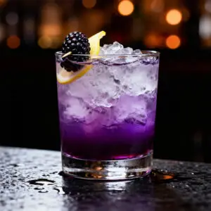 Angled bar-style photo of a bramble cocktail with crushed ice, blackberry garnish, and lemon slice, moody dark background.